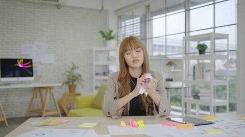 Una joven asiática con exceso de trabajo encuentra un error crítico, arruga el papel con enojo y lo tira