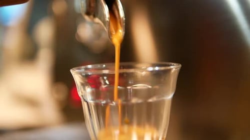 Nahaufnahme einer Kaffeeextraktion, die von der Kaffeemaschine auf das Schnapsglas tropft
