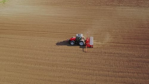 Aerial drone shot of a farmer in tractor seeding, sowing agricultural crops at field.
