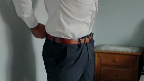 Man adjusting brown belt on trousers, ready for an important moment.