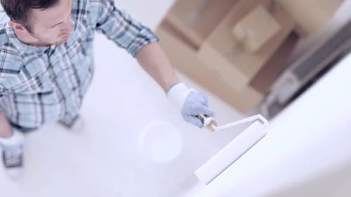 Man painting wall with paint roller indoors