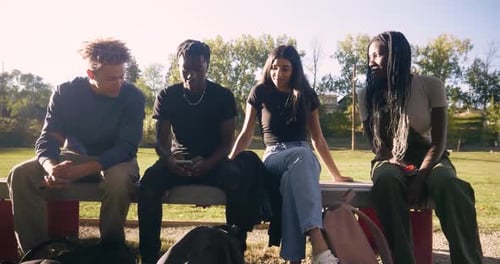 Teenage friends enjoying sunny day at park picnic table with smartphones