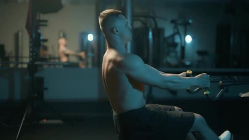 A Handsome Young Muscular Sportsman is Doing Exercise on a Fitness Machine in the Gym