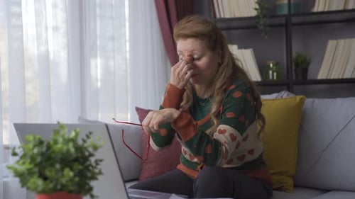 Schmerzen in den Augen. Eine lange berufstätige reife Frau schaut zu Hause auf ihren Laptop.