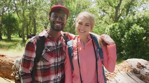Portrait of happy diverse couple with backpacks embracing in park, slow motion