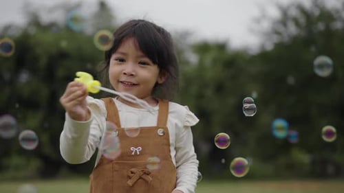 slow motion of happy toddler girl playing soap bubbles in grass field