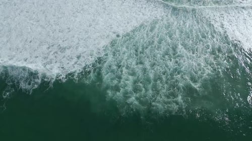 Long aerial top down of powerful ocean waves crashing at the beach. 4k drone shot.