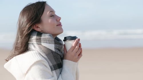 Relaxed Woman Enjoying Coffee on Beach During Winter