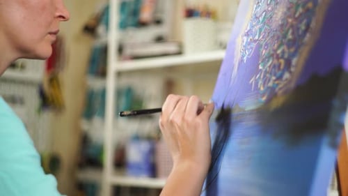 A adult female brunette artist paints a painting on canvas in her creative studio.