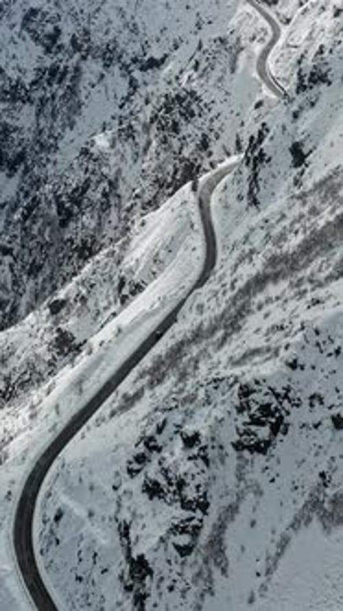 Winding Mountain Road Amidst Snowy Slopes and Rocky Terrain