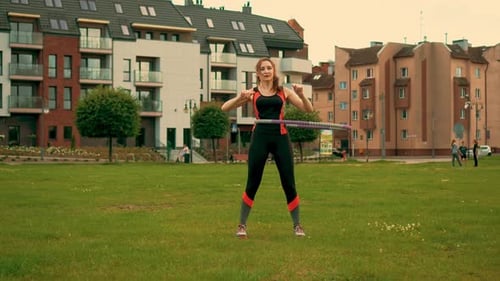 Sexy and Beautiful Caucasian Woman in Sportswear Exercising on Hula Hoop on Green Grass in Urban