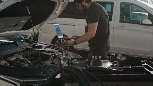 Mechanic with Laptop Performing Diagnostic Work on Car Engine