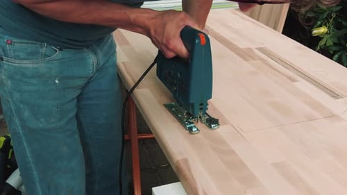 close up man working with smal old jigsaw tool to cut hole into wooden plank