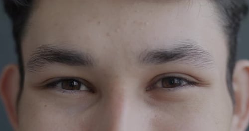 Closeup Portrait of Happy Asian Man's Eyes Looking at Camera Expressing Joy on Gray Color Background