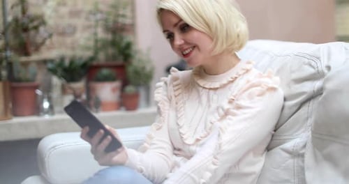 Blonde Woman Relaxing on Sofa Using Mobile Phone
