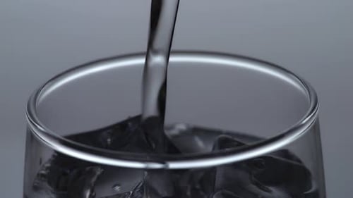 Close Up Of Drinking Water Being Poured Into A Glass With Ice Cubes On The Light White Background