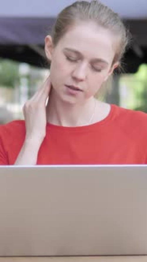 Young Woman with Neck Pain Using Laptop in Cafe Terrace, Vertical Video
