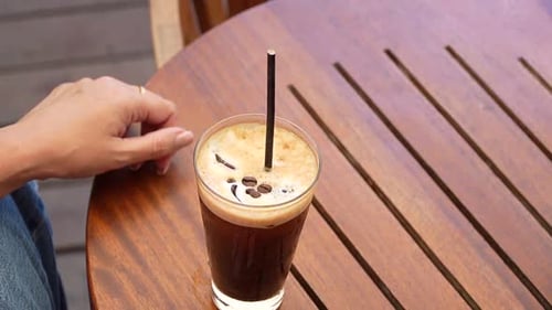 Closeup of Woman with Perfectly Manicured Nails, Touching Straw of Iced Coffee on Sunny Cafe Veranda