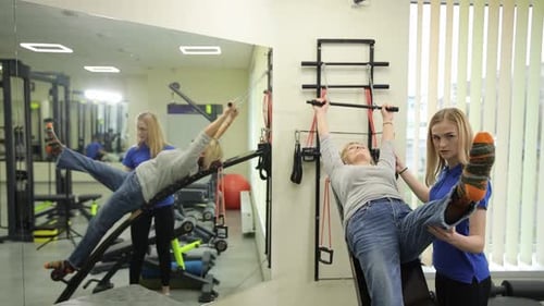 A Young Woman's Personal Trainer Helps an Older Woman Training in a Rehabilitation Center
