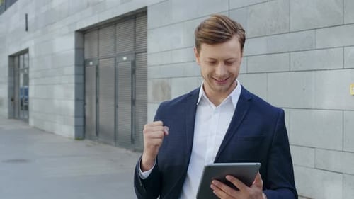 Excited businessman celebrating victory reading good news on digital tablet in city street