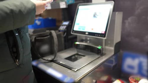 the girl scans the goods at the self-service checkout and pays for the purchase using the phone