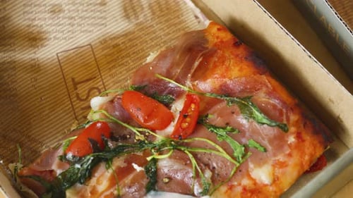 Close up square pizza slice topping prosciutto, arugula, cherry tomatoes, melted
