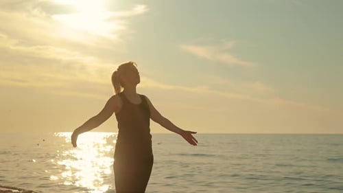 Frau im mittleren Alter macht Atemübungen mit erhobenen Händen und Meditationspraxis am Sunset Beach
