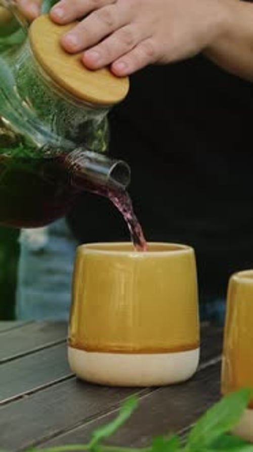 Vertical Video Woman Pouring Red Herbal Tea Into Mug on Wooden Table