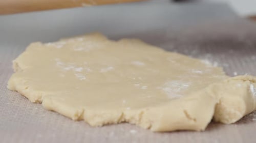 A woman rolls out the dough with a wooden rolling pin, in a close-up view.