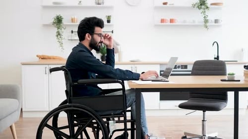 Wheelchair User Typing on Computer in Kitchen Interior