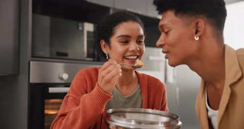 Woman Feeds Man in Kitchen with Spoon