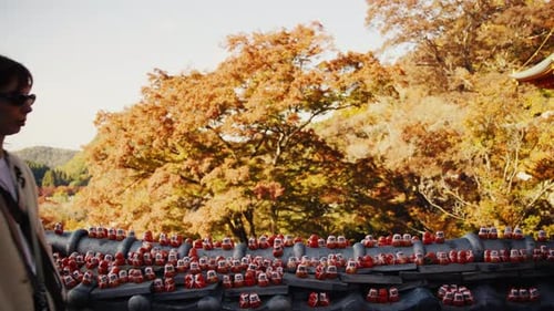 Woman Walking Past Daruma Dolls at Japanese Temple in Autumn