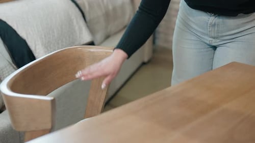 Woman Pulls Wooden Dining Chair to Inspect Seat in Retail Furniture Store