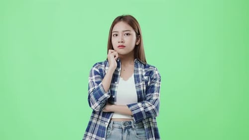 Belle jeune fille asiatique au visage douteux pensant sur fond vert.