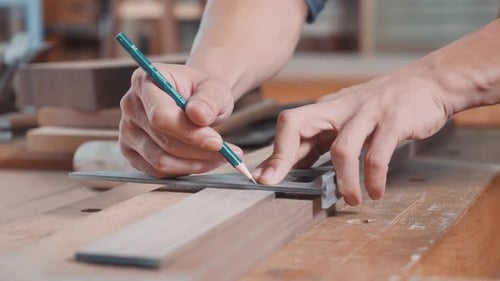 Hands Measuring and Marking Wood Plank with Pencil