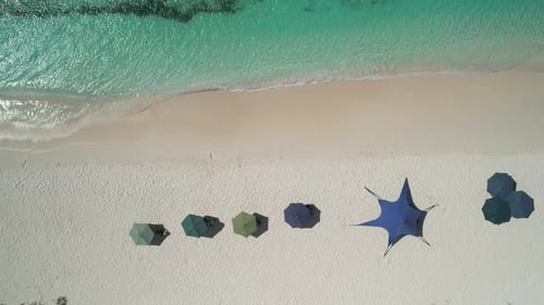 Turquoise waters meeting white sandy beach with colorful umbrellas, aerial view