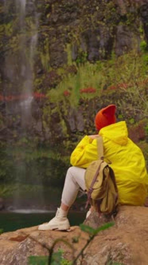 Vertical Video Woman Traveler Hiker in a Yellow Raincoat Near Waterfall in the Highlands Enjoys