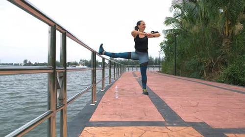 Woman Stretches Leg on Tropical Waterfront Pathway