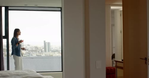 Holding smartphone, woman standing by window in modern home spa setting