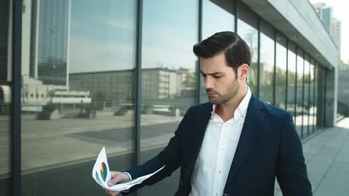 Portrait Of Handsome Businessman Looking Through Documents At Street. Confident Businessman Smili...