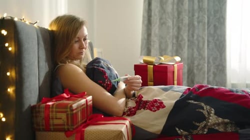 Blonde on Bed with Christmas Gifts Facing Illness During Holidays