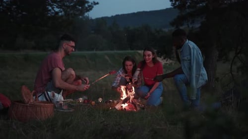 Group of friends cooking food over campfire