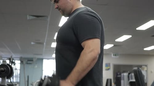 Male performs standing bicep curl in a gym. TILT SHOT.