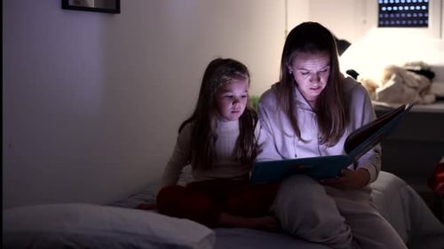 Mother and Daughter Read Book Together at Night