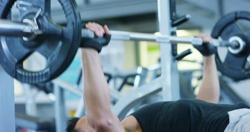 Guy bodybuilder in the gym, works with a barbell, bench press, improving triceps, large pectorals