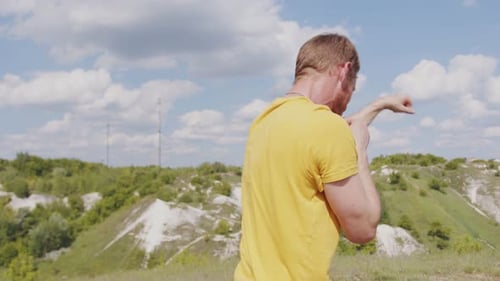 A Man Wearing a Yellow Shirt is Practicing His Boxing Techniques in a Picturesque Park with Lush