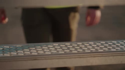 Worker climbing metallic stairs at a construction site during sunset, close-up, outdoor shot