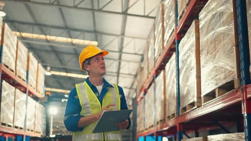 Man worker checks products stock inventory with paper chart in the retail warehouse full of shelves