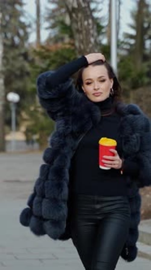 Beautiful young girl in luxury fur coat in the city park.