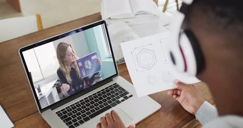 African american male college student holding notes while having a video call on laptop at home